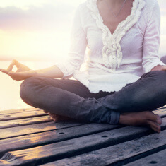 beautiful woman meditating on a boardwalk at sunset